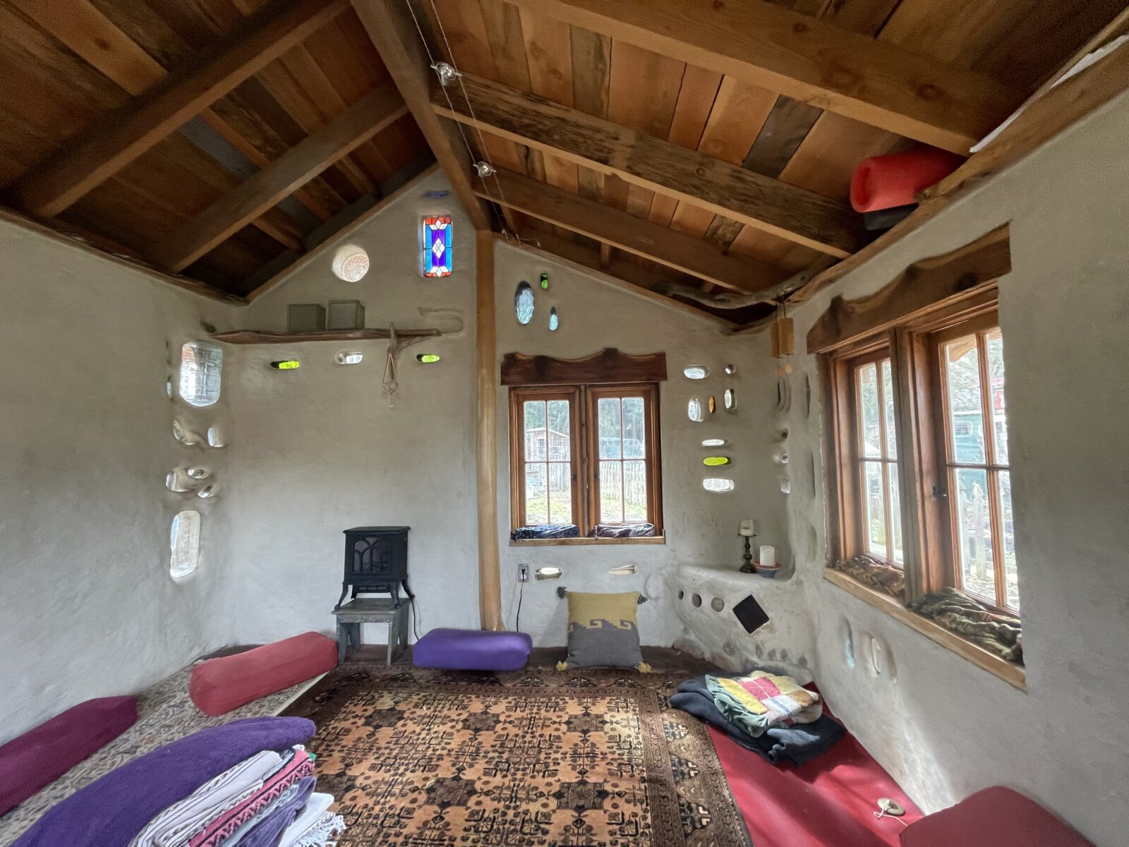 Finished cob interior — stained glass, embedded stones, salvaged wood ceiling
